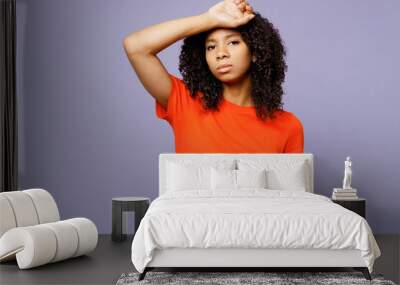 Little tired ill sick kid teen girl of African American ethnicity wear orange t-shirt put hand on forehead suffer from headache isolated on plain pastel purple background. Childhood lifestyle concept Wall mural