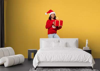 Merry side view little kid teen girl 13-14 years old wear red xmas sweater with deer Santa hat posing holding gift present box isolated on plain yellow background. Happy New Year 2023 holiday concept. Wall mural