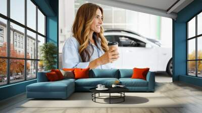 Minded woman customer female buyer client in shirt hold takeaway delivery craft paper cup coffee choose auto want buy new automobile in car showroom vehicle salon dealership store motor show indoor. Wall mural