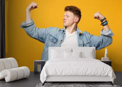 Portrait of strong young man in denim casual clothes looking aside, showing biceps, muscles isolated on yellow orange wall background. People sincere emotions lifestyle concept. Mock up copy space. Wall mural