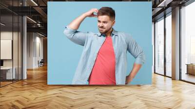 Preoccupied confused young bearded guy in casual shirt posing isolated on pastel blue background studio portrait. People emotions lifestyle concept. Mock up copy space. Put hand on head looking aside. Wall mural