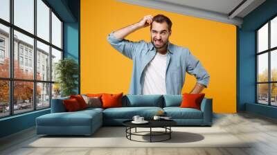 Preoccupied young bearded man in casual blue shirt posing isolated on yellow orange background studio portrait. People emotions lifestyle concept. Mock up copy space. Putting hand on head, looking up. Wall mural