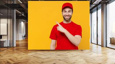 Professional delivery guy employee man in red cap T-shirt uniform workwear work as dealer courier point index finger aside on workspace area isolated on plain yellow background studio Service concept. Wall mural