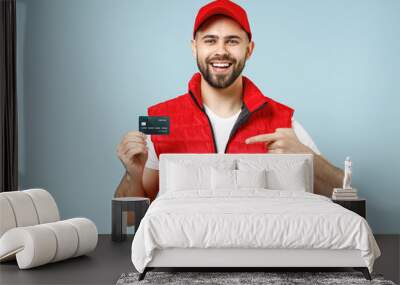 Professional delivery guy employee man in red cap white T-shirt uniform workwear work as dealer courier hold credit bank card isolated on pastel blue color background studio portrait. Service concept. Wall mural