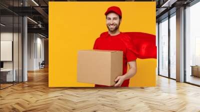 Professional minded delivery guy employee man 20s in red cap T-shirt uniform red cloak workwear work as dealer courier hold cardboard box isolated on plain yellow background studio Service concept Wall mural