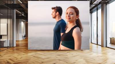 Profile couple young two friend strong sporty sportswoman sportsman woman man in sport clothes warm up training look camera do exercise on sand sea ocean beach outside on seaside in summer day morning Wall mural