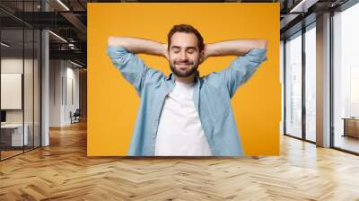 Relaxed young bearded man in casual blue shirt posing isolated on yellow orange background studio portrait. People sincere emotions lifestyle concept. Mock up copy space. Sleep with hands behind head. Wall mural