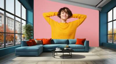 Relaxed young brunette woman girl in yellow sweater posing isolated on pastel pink wall background, studio portrait. People lifestyle concept. Mock up copy space. Sleeping with hands behind head. Wall mural