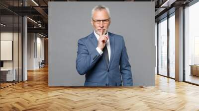 Secret elderly gray-haired bearded business man in blue suit shirt tie isolated on grey background . Achievement career wealth business concept. Saying hush be quiet with finger on lips shhh gesture. Wall mural