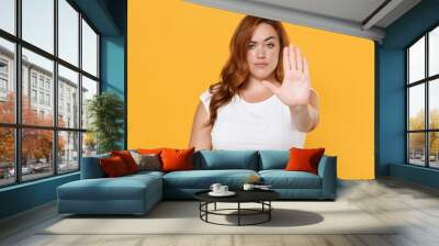 Serious young redhead plus size body positive female woman girl 20s in white blank design casual t-shirt posing showing stop gesture with palm isolated on yellow color background studio portrait. Wall mural