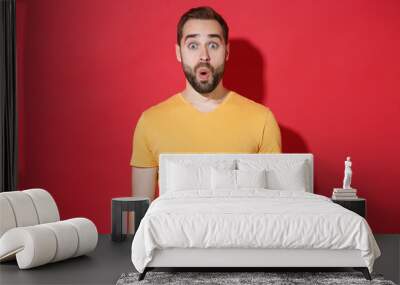 Shocked amazed young bearded man guy in casual yellow t-shirt posing isolated on red wall background studio portrait. People sincere emotions lifestyle concept. Mock up copy space. Keeping mouth open. Wall mural