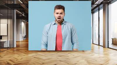 shocked perplexed young bearded guy in casual shirt posing isolated on pastel blue background studio Wall mural