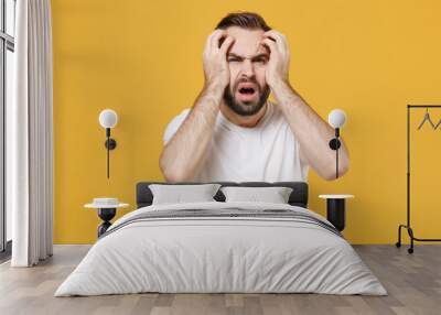 Shocked tired young bearded man guy in white casual t-shirt posing isolated on yellow wall background studio portrait. People sincere emotions lifestyle concept. Mock up copy space. Put hands on head. Wall mural