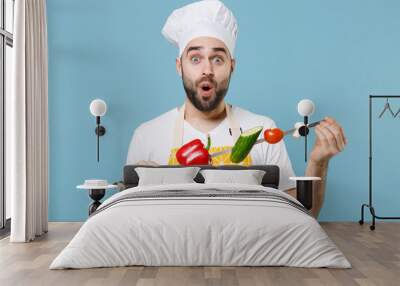 Shocked young bearded male chef cook man in apron white t-shirt toque chefs hat isolated on blue background studio portrait. Cooking food concept. Mock up copy space Hold skewer with fresh vegetables. Wall mural