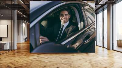 Side profile view young driver confident smiling businessman man 20s wear black dinner suit driving car taxi hold steering wheel look camera Vehicle transport traffic lifestyle business trip concept Wall mural