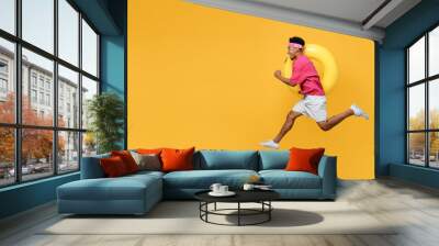 Side view happy fun cool young man he wear pink t-shirt near hotel pool jump high run fast hurrying up hold inflatable rubber ring isolated on plain yellow background Summer vacation sea rest concept Wall mural