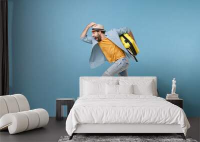 Side view of excited traveler tourist man in yellow clothes isolated on blue background. Male passenger traveling abroad on weekends. Air flight journey concept. Jumping like running, hold suitcase. Wall mural