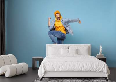 Side view of happy young hipster guy in fashion jeans denim clothes posing isolated on pastel blue background studio portrait. People lifestyle concept. Mock up copy space. Jump doing winner gesture. Wall mural