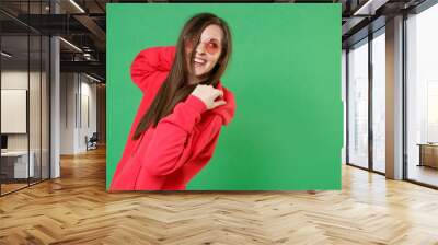 Side view of smiling cheerful laughing beautiful young brunette woman 20s in bright red casual streetwear hoodie eyeglasses posing looking aside isolated on green color background studio portrait. Wall mural