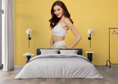 Side view smiling sexy lovely attractive young brunette woman 20s in white underwear with perfect fit body standing posing looking camera isolated on plain yellow color background studio portrait Wall mural