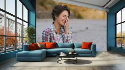 Side view young happy fun cheerful woman wear shirt casual clothes put hand on face laugh smiling sits rest on sea ocean sand shore beach outdoor seaside in summer day free time. Lifestyle concept. Wall mural