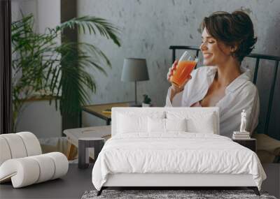 Side view young smiling woman wear white shirt pajama she lying in bed eat breakfast drink orange juice rest relax spend time in bedroom lounge home in own room hotel wake up dream in good mood day Wall mural