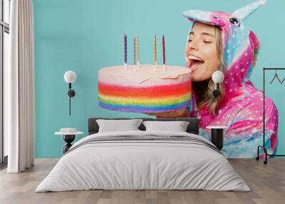 Side view young woman in domestic costume with hoody and animals ears hold in hand birthday cake with candles biting making wish isolated on plain pastel light blue cyan background Lifestyle concept Wall mural