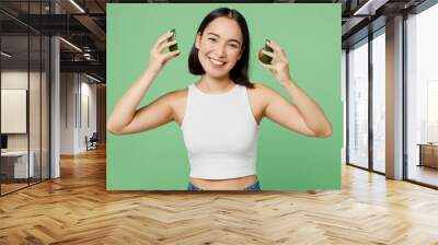 Side view young woman wear white clothes hold two halves of avocado pov headphones near ears isolated on plain pastel light green background Proper nutrition healthy fast food unhealthy choice concept Wall mural