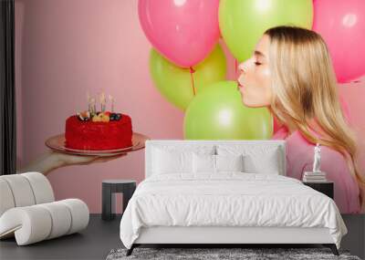 Side view young woman wears shirt celebrating birthday holiday and hold bunch of colorful air balloons, red cake blow out candles making wish isolated on plain light pink background Lifestyle concept Wall mural