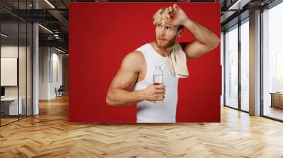 Sideways young strong sporty sportsman man in white clothes towel on shoulder wipe sweat spend time in home gym look aside drink water isolated on plain red background Workout sport fit body concept Wall mural