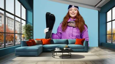 Skier satisfied happy fun cool sporty woman in warm purple padded windbreaker jacket goggles mask spend extreme weekend in mountains hold ski sport equipment isolated on plain blue background studio Wall mural