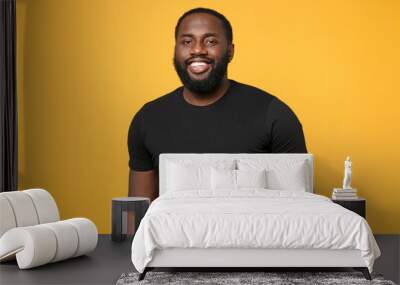 Smiling african american man guy football fan in casual black t-shirt isolated on yellow wall background studio portrait. People sincere emotions lifestyle concept. Mock up copy space. Looking camera. Wall mural