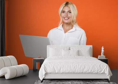 Smiling beautiful attractive young blonde female business woman girl 20s wearing white shirt posing working on laptop pc computer isolated on bright orange color wall background studio portrait. Wall mural