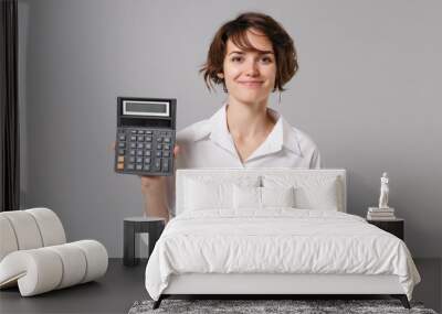 Smiling beautiful young business woman in white shirt posing isolated on grey wall background studio portrait. Achievement career wealth business concept. Mock up copy space. Hold in hand calculator. Wall mural