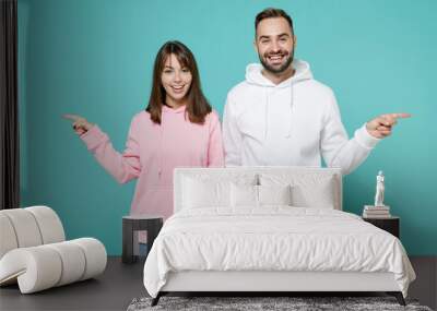 Smiling cheerful young couple two friends man woman 20s wearing white pink casual hoodie pointing index fingers aside looking camera isolated on blue turquoise colour wall background studio portrait. Wall mural