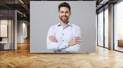 Smiling confident young unshaven business man in light shirt posing isolated on grey background studio portrait. Achievement career wealth business concept. Mock up copy space. Holding hands crossed. Wall mural