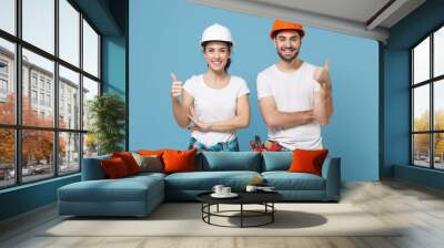 Smiling couple woman man in casual clothes protective helmet hardhat isolated on blue background studio. Instruments accessories for renovation apartment room. Repair home concept. Showing thumbs up. Wall mural