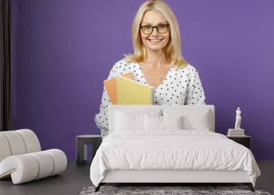 Smiling gray-haired blonde teacher woman lady 40s 50s years old wearing white dotted blouse eyeglasses standing hold notepads looking camera isolated on bright violet color background studio portrait. Wall mural