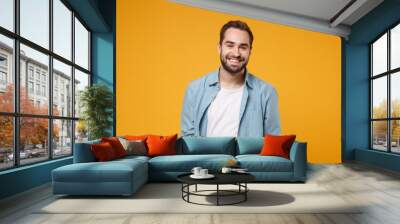 Smiling handsome young bearded man in casual blue shirt posing isolated on yellow orange wall background studio portrait. People sincere emotions lifestyle concept. Mock up copy space. Looking camera. Wall mural