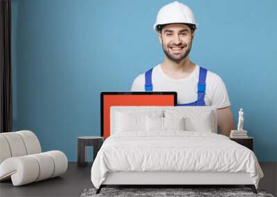 Smiling man in coveralls protective helmet hardhat hold laptop computer with blank empty screen isolated on blue background. Instruments accessories for renovation apartment room. Repair home concept. Wall mural