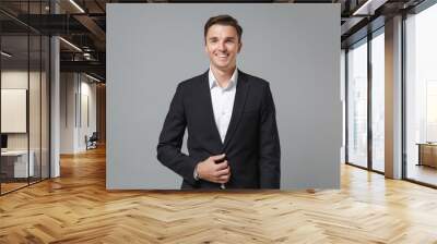 Smiling successful young business man in classic black suit shirt posing isolated on grey background studio portrait. Achievement career wealth business concept. Mock up copy space. Looking camera. Wall mural