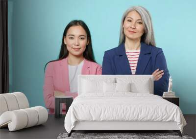 Smiling two asian female business women employer employee in pink blue jackets posing working in office looking camera holding hands crossed isolated on pastel blue color background studio portrait. Wall mural