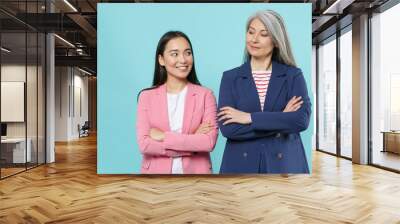 Smiling two asian female business women employer employee in pink blue jackets working in office looking at each other holding hands crossed isolated on pastel blue color background studio portrait. Wall mural