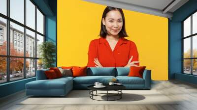 Smiling vivid young woman of Asian ethnicity 20s years old wears orange shirt looking camera hold hands crossed isolated on plain yellow background studio portrait. People emotions lifestyle concept. Wall mural