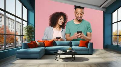 Smiling young african american couple two friends guy girl in gray green casual clothes posing using mobile cell phone typing sms message isolated on pastel pink color wall background studio portrait. Wall mural