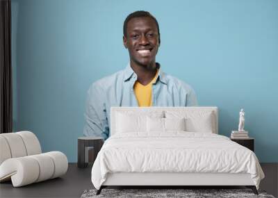 Smiling young african american man guy in casual shirt, yellow t-shirt posing isolated on blue wall background. People lifestyle concept. Mock up copy space. Using mobile phone, typing sms message. Wall mural