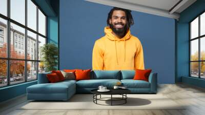 Smiling young african american man guy wearing casual yellow streetwear hoodie posing isolated on blue wall background studio portrait. People sincere emotions lifestyle concept. Looking camera. Wall mural