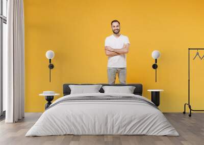 Smiling young bearded man guy in white casual t-shirt posing isolated on yellow wall background studio portrait. People sincere emotions lifestyle concept. Mock up copy space. Holding hands crossed. Wall mural