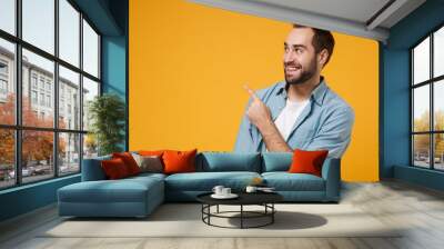 Smiling young bearded man in casual blue shirt posing isolated on yellow orange background studio portrait. People sincere emotions lifestyle concept. Mock up copy space. Pointing index finger up. Wall mural