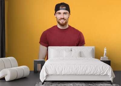 Smiling young bearded tattooed man guy in casual t-shirt, black cap posing isolated on yellow wall background studio portrait. People emotions lifestyle concept. Mock up copy space. Looking camera. Wall mural